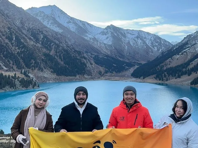 Vier mensen houden een gele banner vast voor het Grote Almaty-meer.