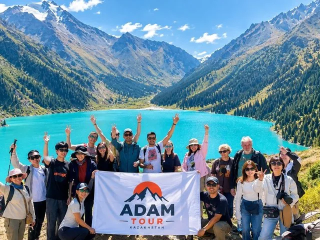 Een grote groep mensen poseert met een spandoek bij het Grote Almaty-meer.