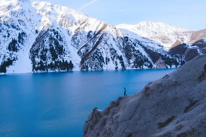 Eine Person steht auf einem Felsvorsprung mit Blick auf den Großen Almaty-See.