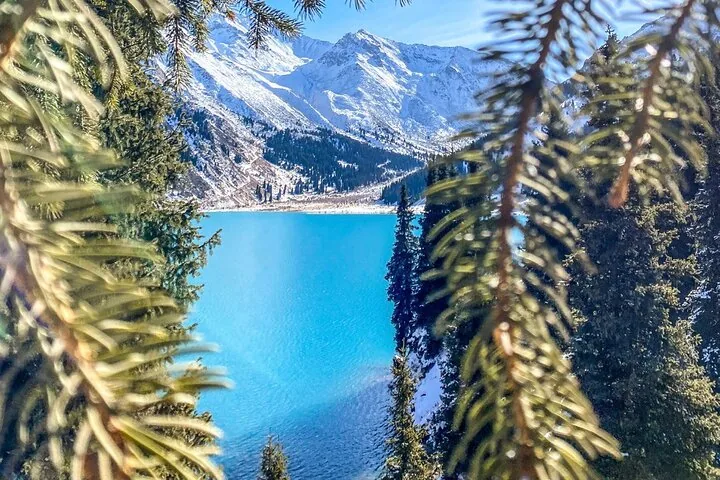 Vue du Grand lac d'Almaty partiellement encadrée par des branches de pins.